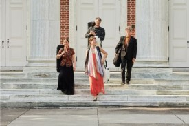 String quartet with instruments in cases descend stairs outside brick and stone auditorium